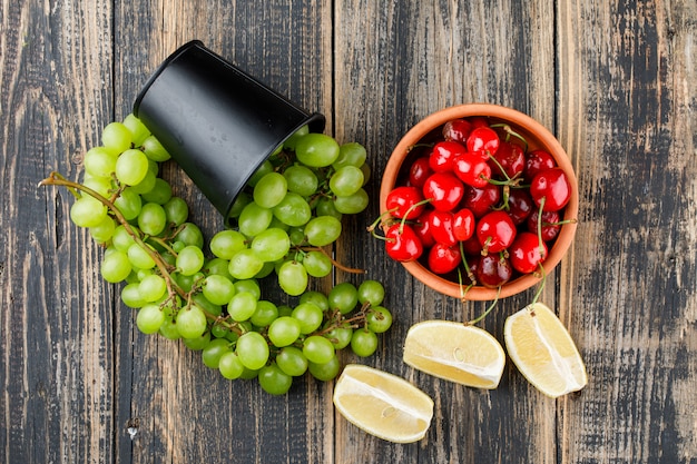 Free photo scattered grapes from a mini bucket with lemon slices, cherries top view on a wooden surface