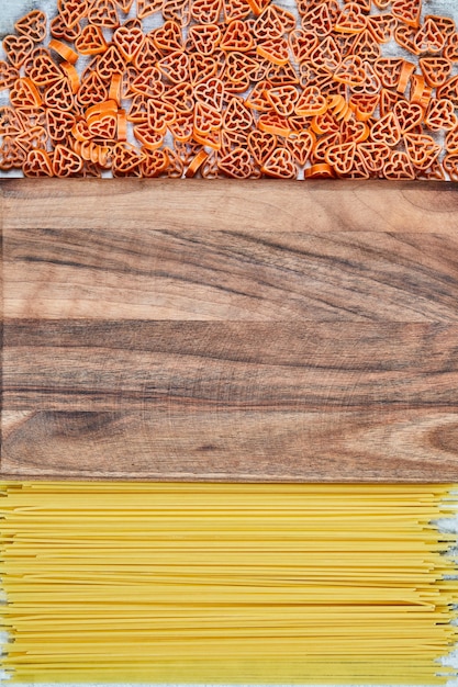 Scattered heart-shaped pasta and spaghetti around the wooden board.