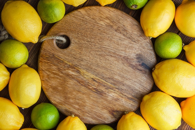 Free photo scattered lemons with limes on wooden and cutting board, flat lay.