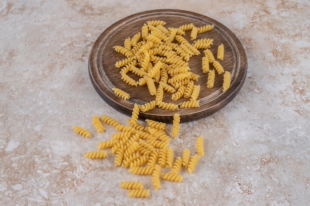 Scattered portion of raw pasta on a wooden board and on marble surface.