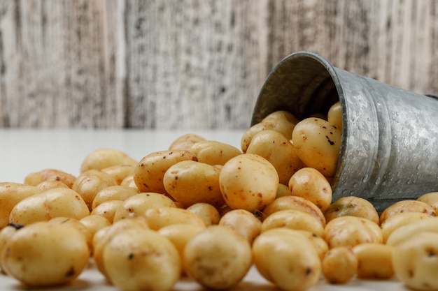 Scattered potatoes from a mini bucket on white and grungy wooden wall. side view.