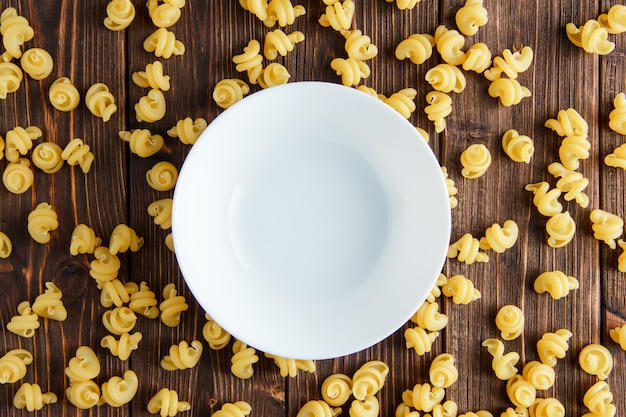 Scattered raw pasta with empty plate flat lay on a wooden table