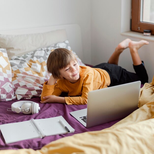 School boy sitting in bed with his laptop