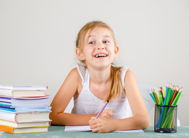 School concept with pencils, books, copybooks side view. little girl holding pencil.