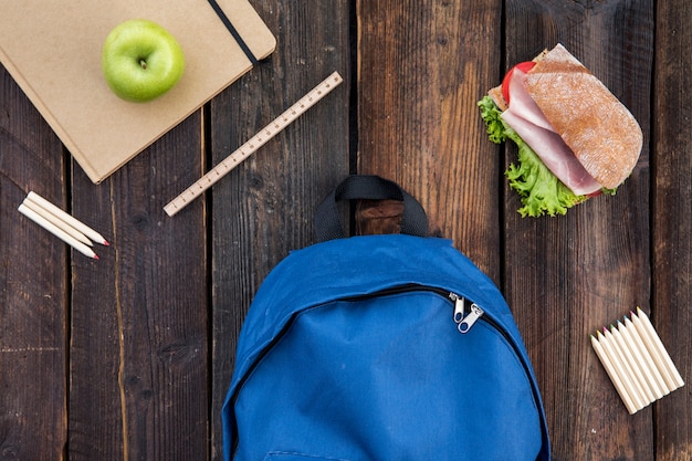 Schoolbag, sandwich and stationery on table