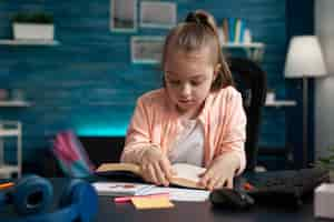 Free photo schoolchild sitting at desk in living room holding school book