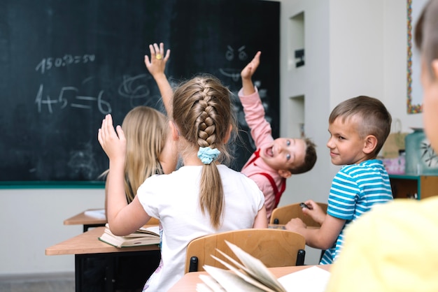 Free photo schoolchildren sitting in classroom raising hands