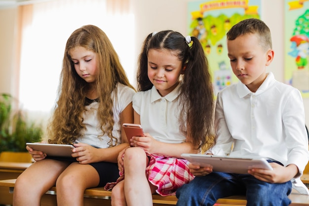 Free photo schoolchildren sitting on desk with gadgets