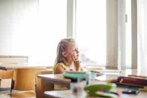 Free photo schoolgirl sitting at desk touching cheek