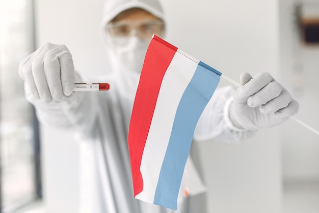 Free photo the scientist in coverall suit with a coronavirus sample and the netherlands' flag