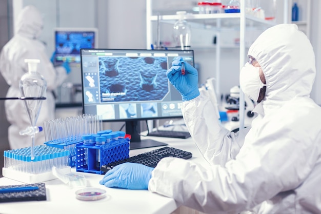 Scientist in protection suit holding sample of infected blood with coronavirus in test tube