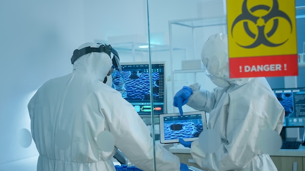 Scientists in coverall standing behind the glass wall working in danger area of lab