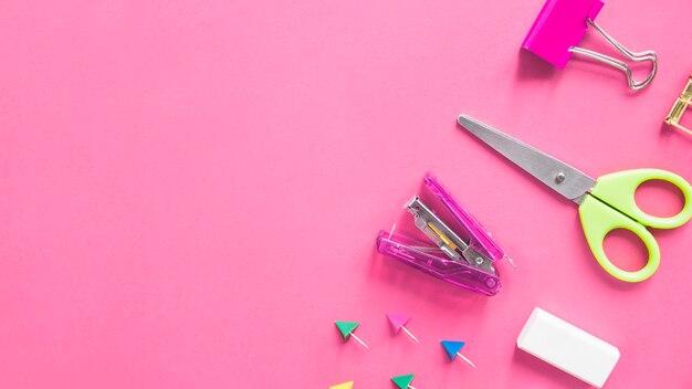 Scissors; stapler; bulldog clip; eraser and push pins on pink background