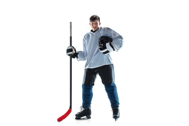 Scoring. Young male hockey player with the stick on ice court and white background. Sportsman wearing equipment and helmet practicing. Concept of sport, healthy lifestyle, motion, movement, action.