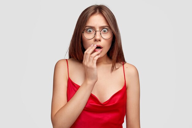 Scraed brunette young woman posing against the white wall