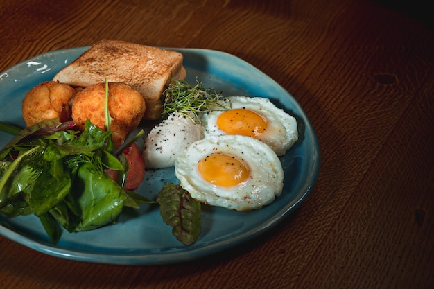 Free photo scrambled eggs on meat with fried potatoes and toast at plate on wooden table