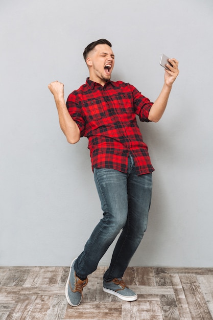 Screaming young man using mobile phone make winner gesture.