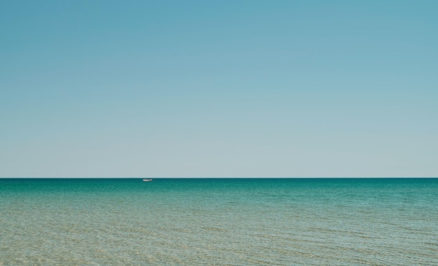 Sea panorama in shallow water with sun reflection in water vast open sea with clear sky ripple wave and calm sea with beautiful sunlight Red boat is visible in distance Wallpaper or banner idea