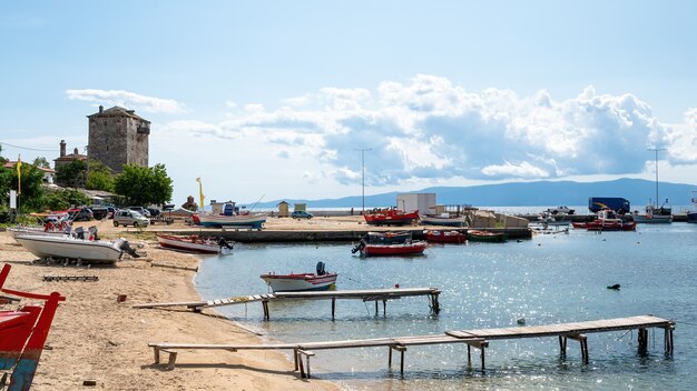 Sea port, moored boats on Aegean sea, few parked cars, two small wooden piers and Tower of Prosphorion, Ouranoupolis, Greece