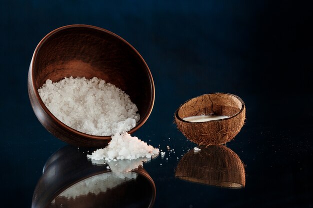 Sea salt in wooden bowl and coconut over black surface