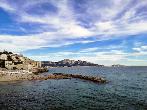 Free photo sea surrounded by buildings and hills under a cloudy sky and sunlight in marseille in france