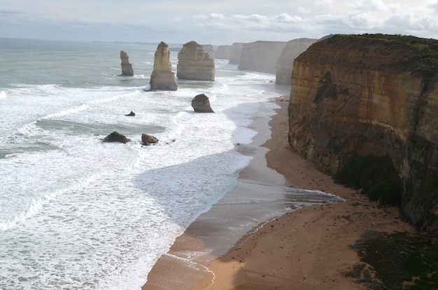 Free photo sea waves hitting the shore with rocks near cliffs under a cloudy sky