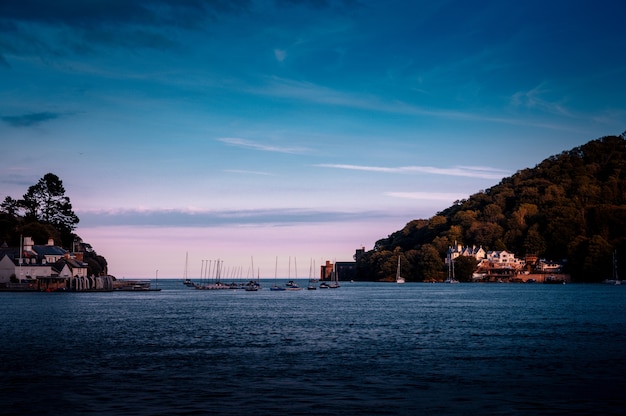 Free photo a sea with ships and  buildings on the coast surrounded by high green mountains in dartmouth, uk