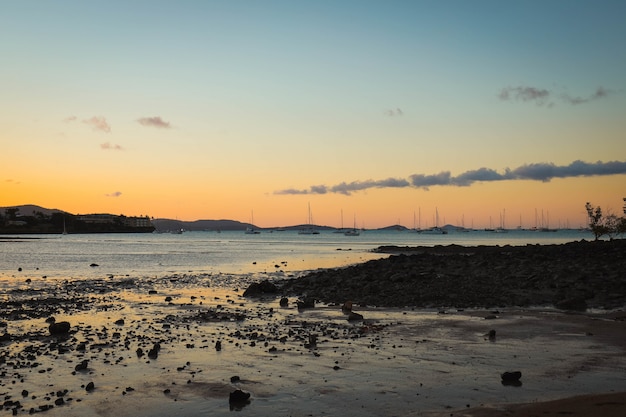 Sea with ships on it surrounded by the beach and hills during the sunset in the evening