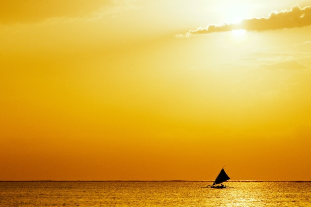 Free Photo seascape with golden sunset and a sailboat in the middle of the ocean