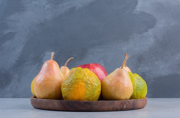 Seasonal fruits on wooden plate on grey background. 