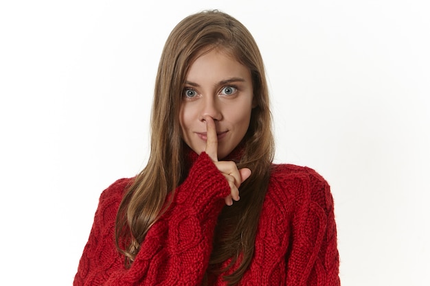 Free Photo secrecy, conspiracy and confidential information concept. isolated image of attractive mysterious young lady in sweater making shh geture with fore finger at lips, asking to keep her secret