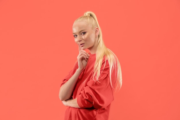 Secret, gossip concept. Young woman whispering a secret behind her hand. Business woman isolated on trendy coral studio background. Young emotional woman. Human emotions, facial expression concept.