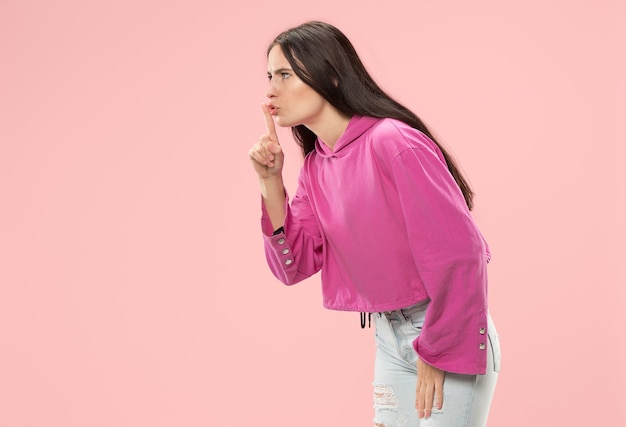 Secret, gossip concept. Young woman whispering a secret behind her hand. Business woman isolated on trendy pink  wall. Young emotional woman. Human emotions, facial expression concept.