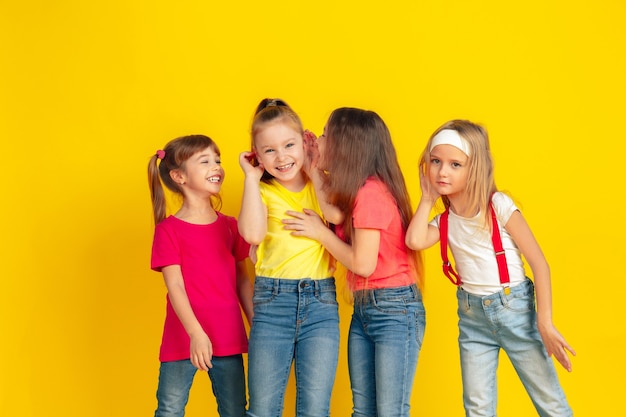 Free photo secrets. happy children playing and having fun together on yellow studio background. caucasian kids in bright clothes looks playful, laughting, smiling. concept of education, childhood, emotions.