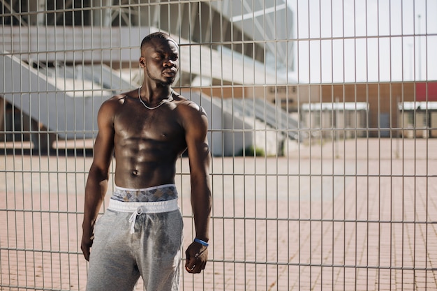 Seductive African American man with muscels poses with naked chest before the fence