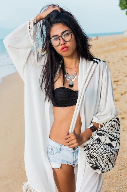 Free photo seductive asian woman in black top and jeans shorts , beach cover up with boho bag posing on tropical beach. bohemian woman enjoying weekends. perfect body.jewelry , bracelet and necklace.