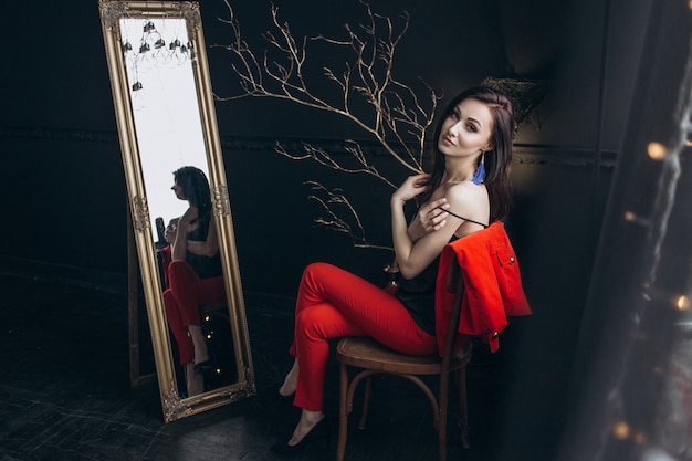 Seductive woman in red suit sits before a mirror