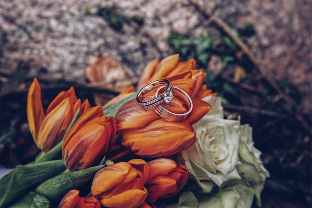 Selective closeup shot of silver diamond rings on orange tulips and white roses