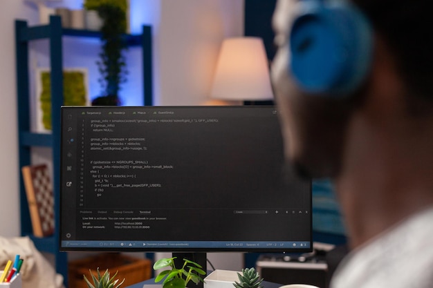 Selective focus on african american it employee with headset working remote from home at website design using programming technologies on computer. Programmer man coding digital business server