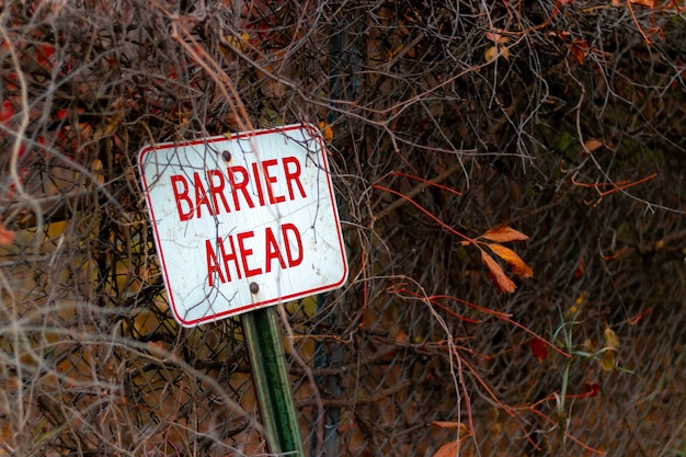 Free photo selective focus shot of a barrier ahead sign leaned against a metal fence