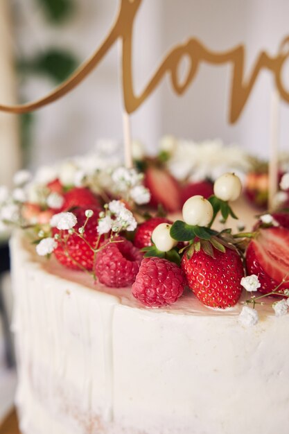 Selective focus shot of delicious white wedding cake with red berries, flowers and cake topper