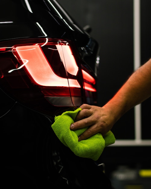 Free photo selective focus shot of a man cleaning car's back headlight with a microfiber cloth