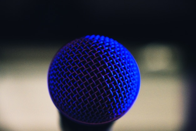 Selective focus shot of a microphone net reflecting blue light from the stage