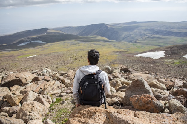 Selective focus shot of a person sitting on a rock with a beautiful view of mountains