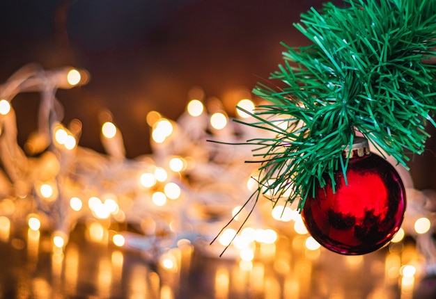 Selective focus shot of a red Christmas ball on a pine tree with lights on the background