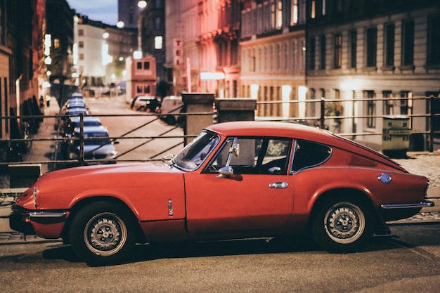 Selective focus shot of a red Porsche car parked near buildings in a blurry background