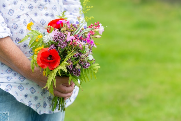 Free photo selective focus shot of someone holding a bouquet of different flowers outdoors during daylight