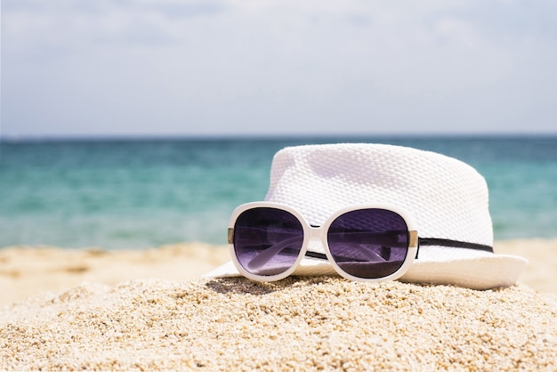 Free photo selective focus shot of sunglasses and a white hat on a sandy beach