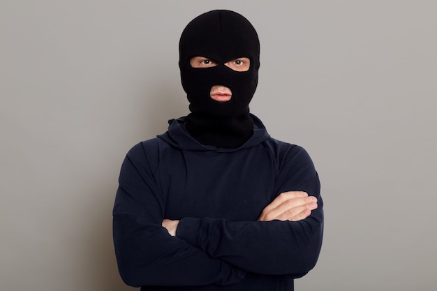 Self-confident criminal male posing isolated on a gray surface