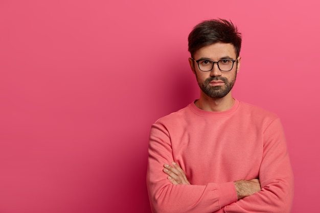 Self confident serious bearded man stands with arms folded